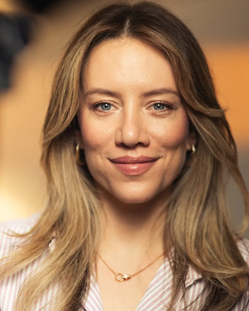 Retrato de Lívia Oliveira em close, sorrindo de leve, com fundo em tons quentes